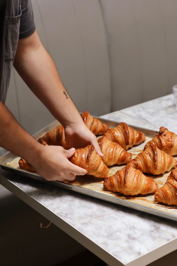 Hands arranging fresh croissants on a baking tray