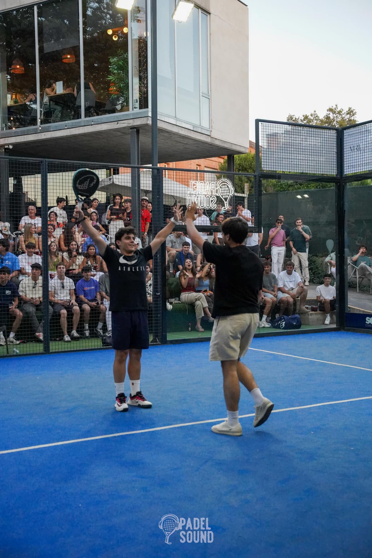 Jugadores celebrando un high-five ante la grada repleta al atardecer en Padel Sound 005