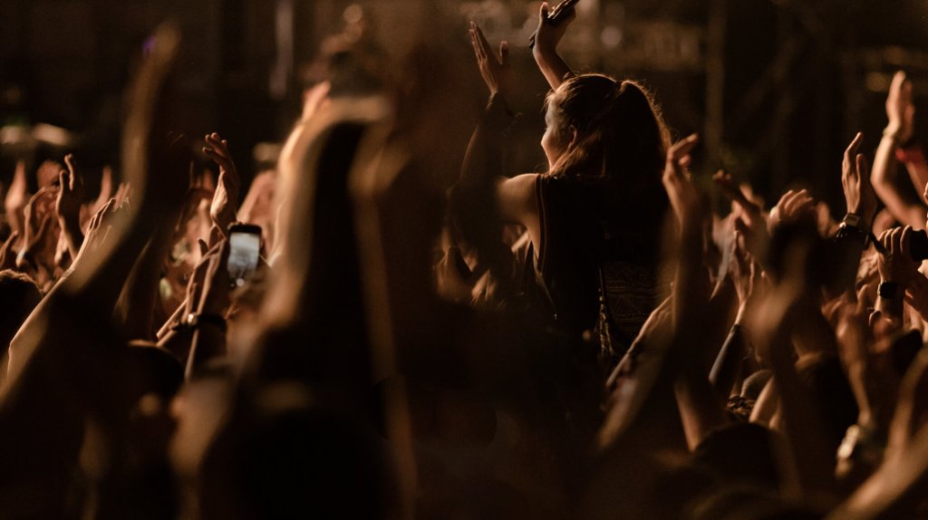 Concert audience with hands raised under warm stage lights