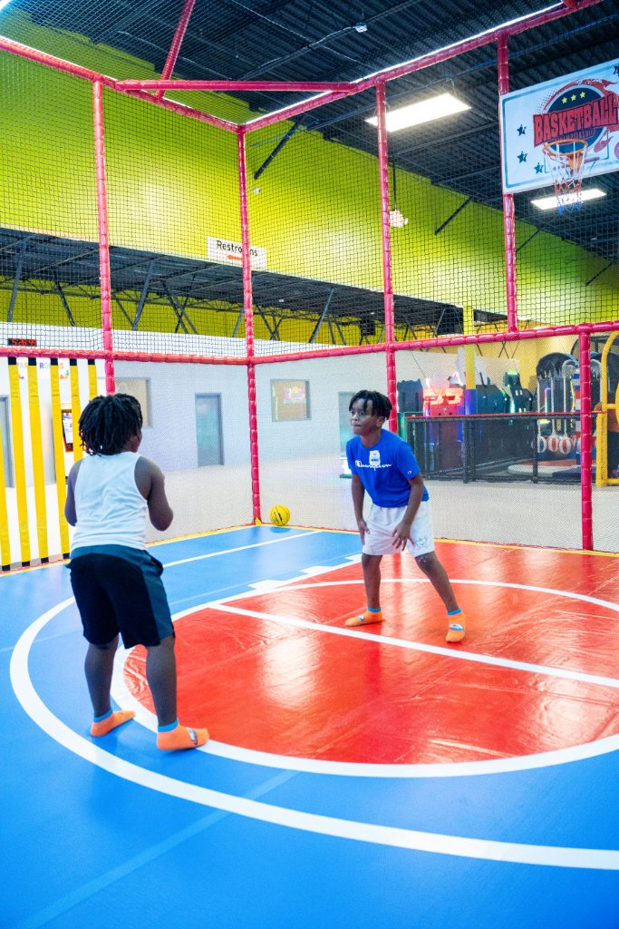 Two boys playing basketball inside a netted court with padded walls at Lululand Adventure Park