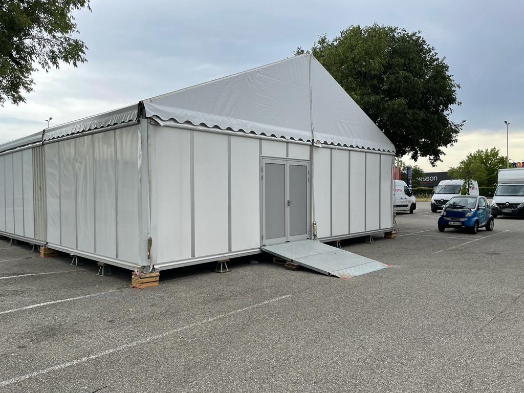 Chapiteau bardé avec porte et rampe d'accès sur parking