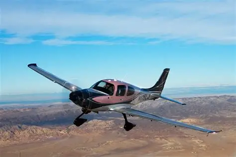 Pink and silver Cirrus aircraft banking over a mountainous desert landscape