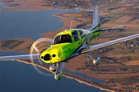 Lime green and silver Cirrus aircraft in flight over water and fields