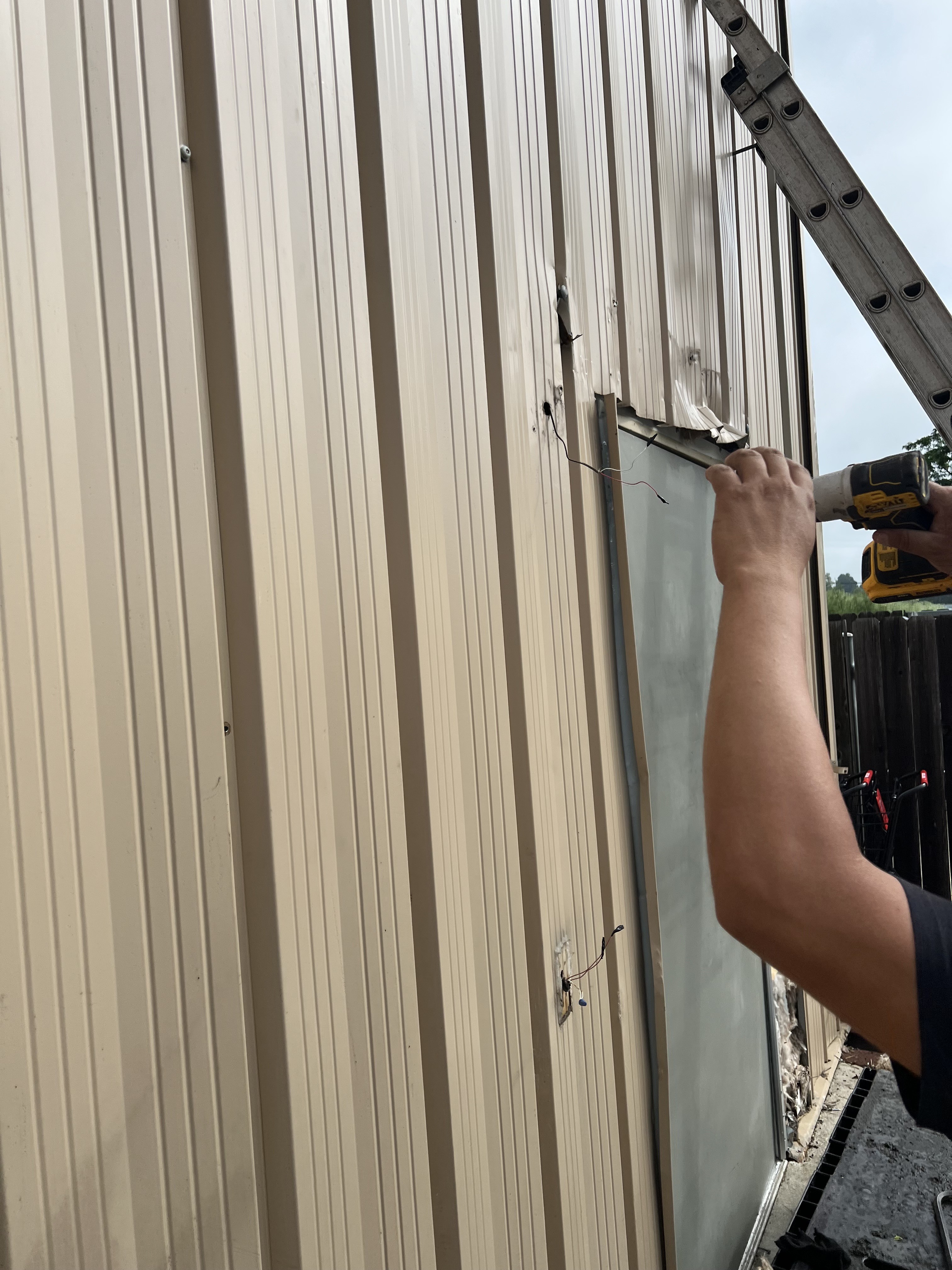 Real TNT Roofing commercial project: crew member installing vertical metal siding panels on a dollar store exterior using a power drill