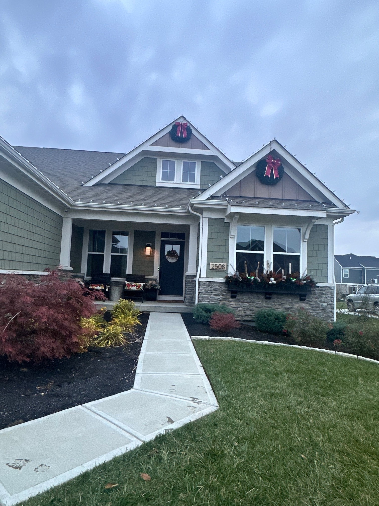 Real TNT Roofing project: two-story home with sage green James Hardie HardieShingle siding, white trim, and stacked stone veneer accents