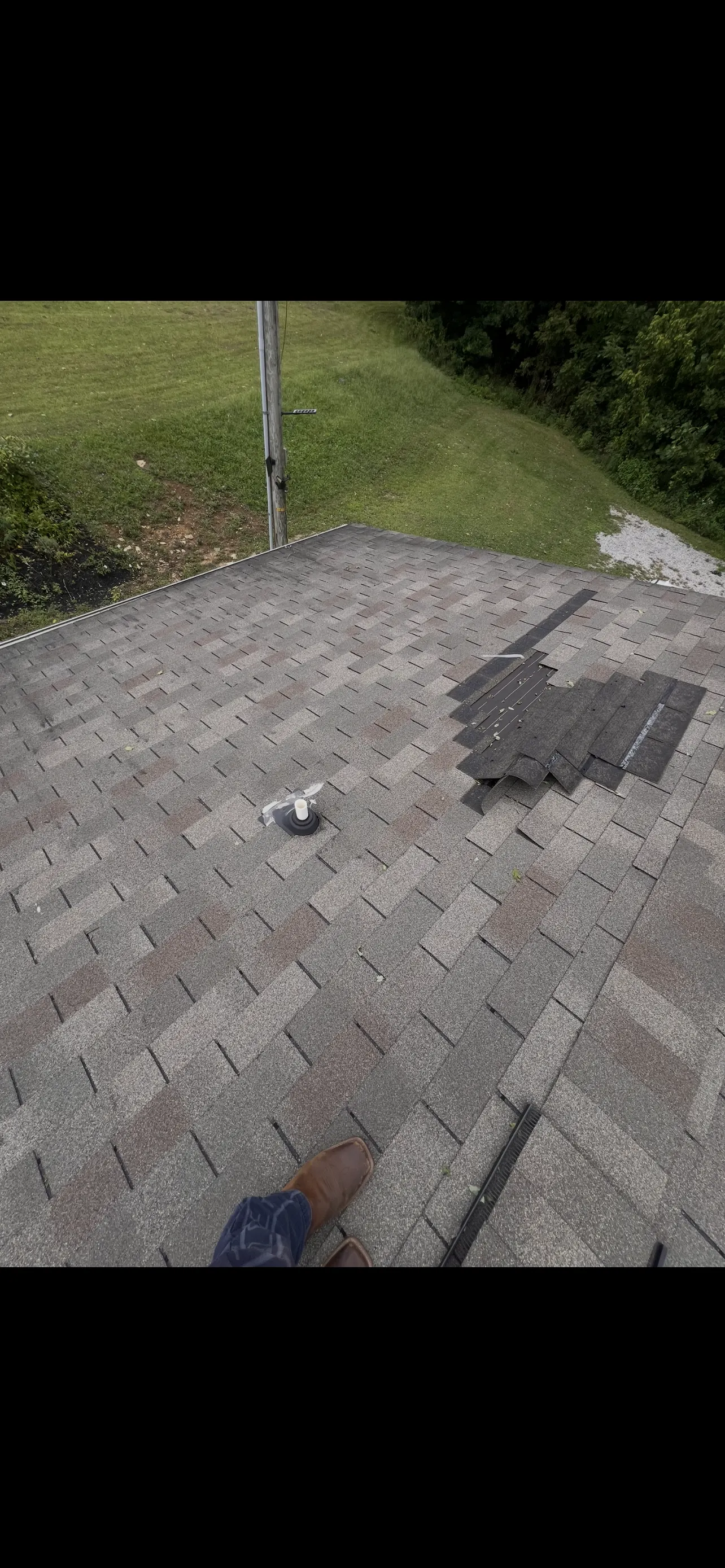 Storm-damaged asphalt shingles torn and folded back, exposing underlayment and decking on a residential roof — before emergency tarping