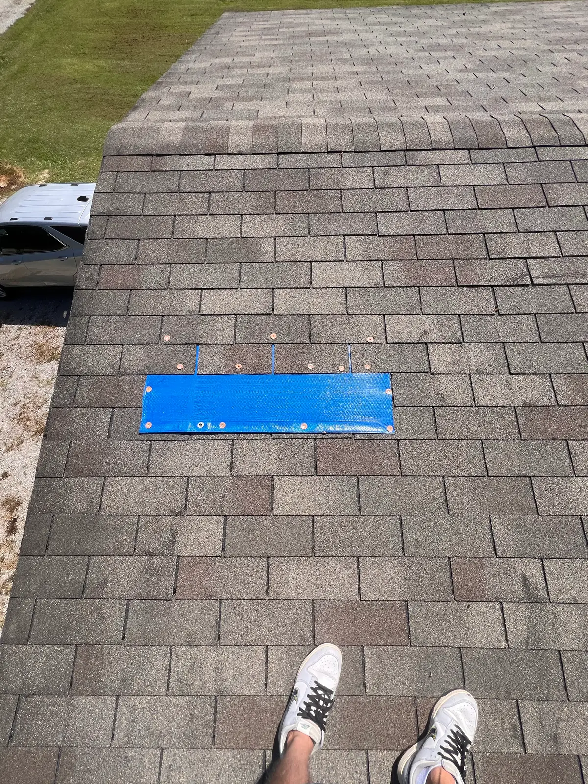 Blue emergency tarp secured over the damaged roof area with metal fasteners — temporary storm damage protection by TNT Roofing
