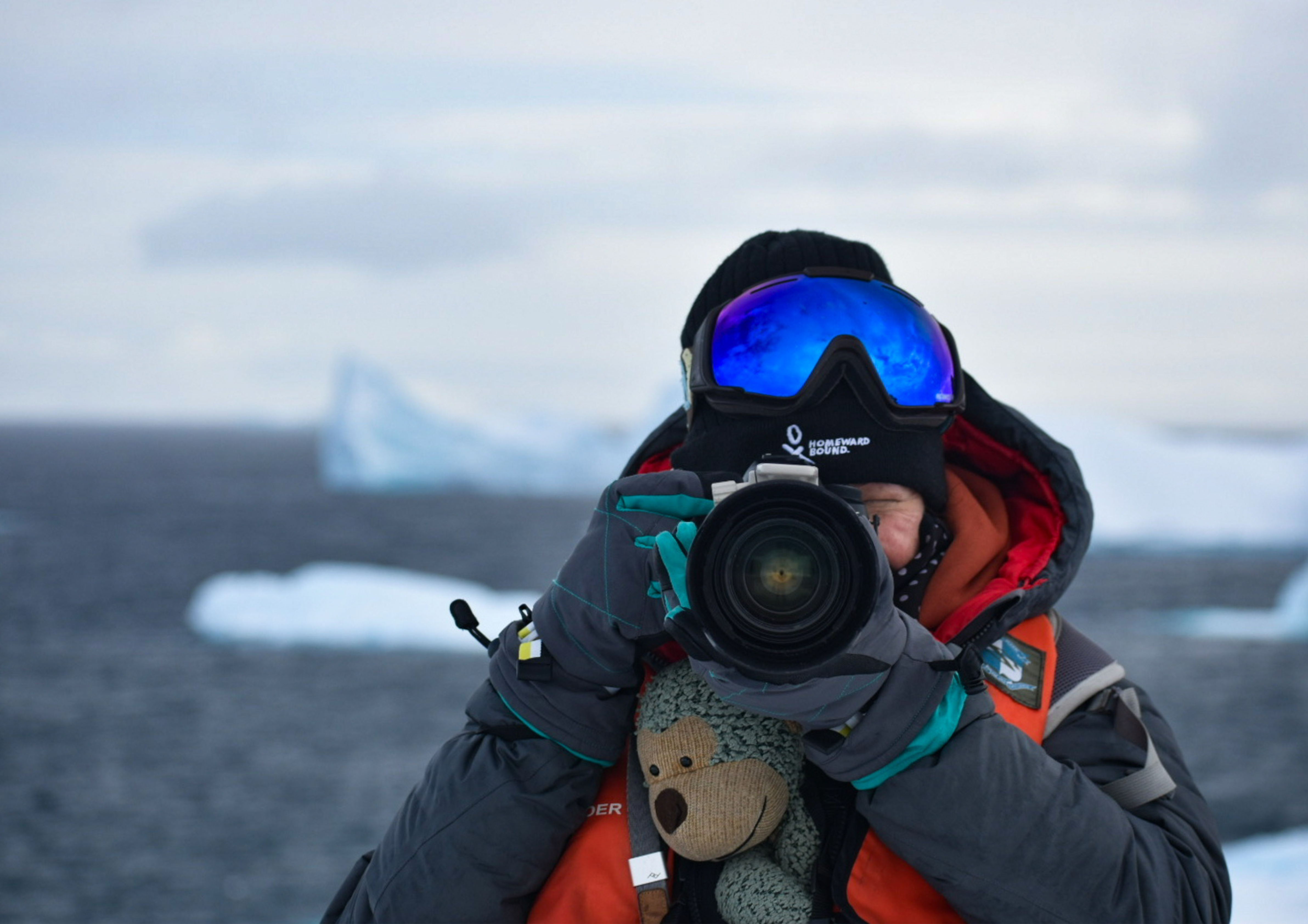 Jodi Salmond in Antarctica holding a camera with a plush monkey mascot