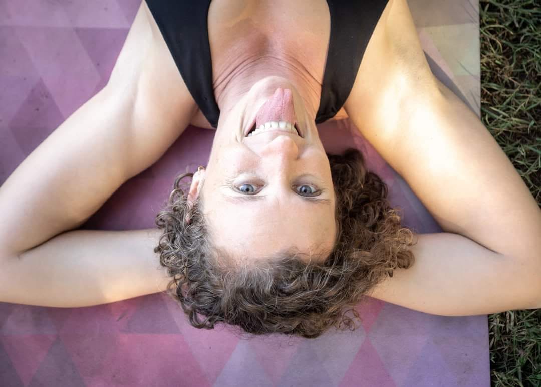Gabriella Salmon lying on a mat outdoors, smiling and getting ready to play during an acro or movement session.
