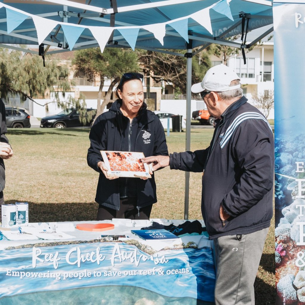Jodi Salmond and a community member looking at a framed coral photo together at a Reef Check Australia outdoor booth.