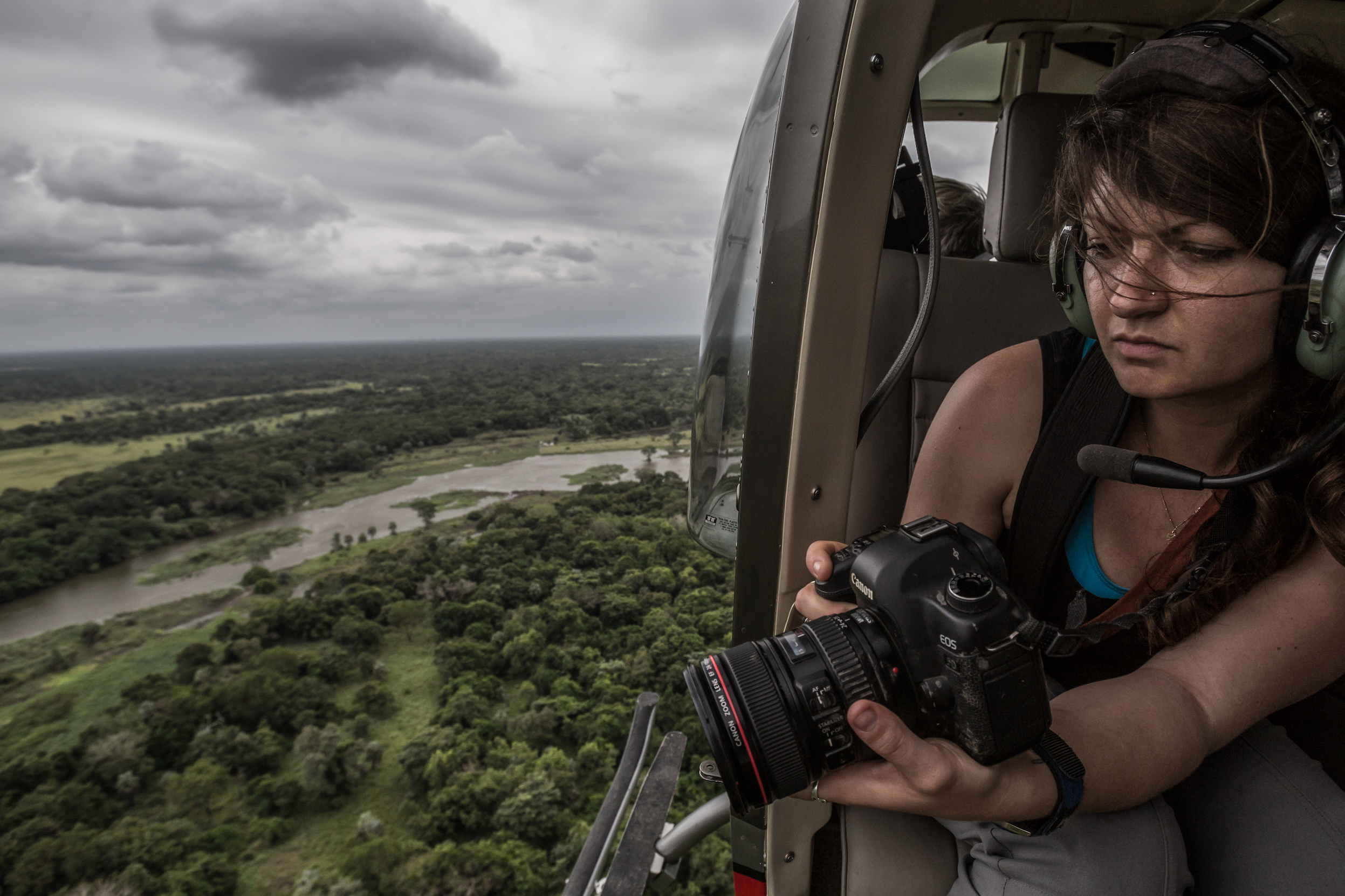 Jen Guyton looking through a camera lens inside a helicopter over a lush green landscape