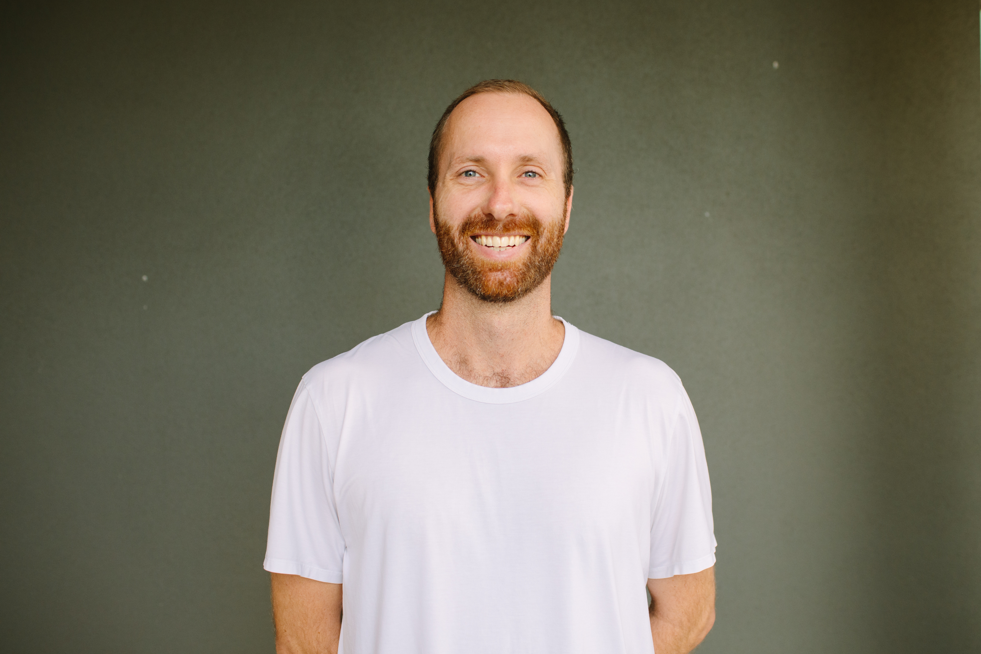 Ryan Griffin smiling in a white t-shirt against a muted green backdrop