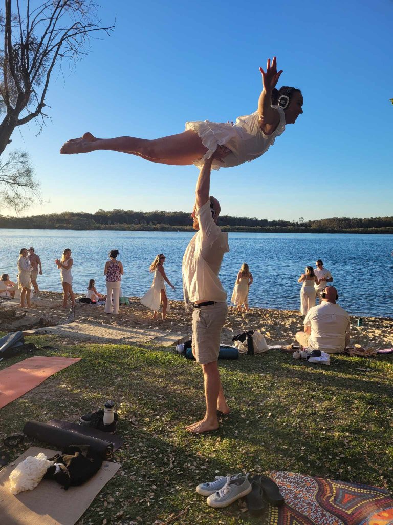 Two people practising partner acrobatics outdoors by the water at golden hour