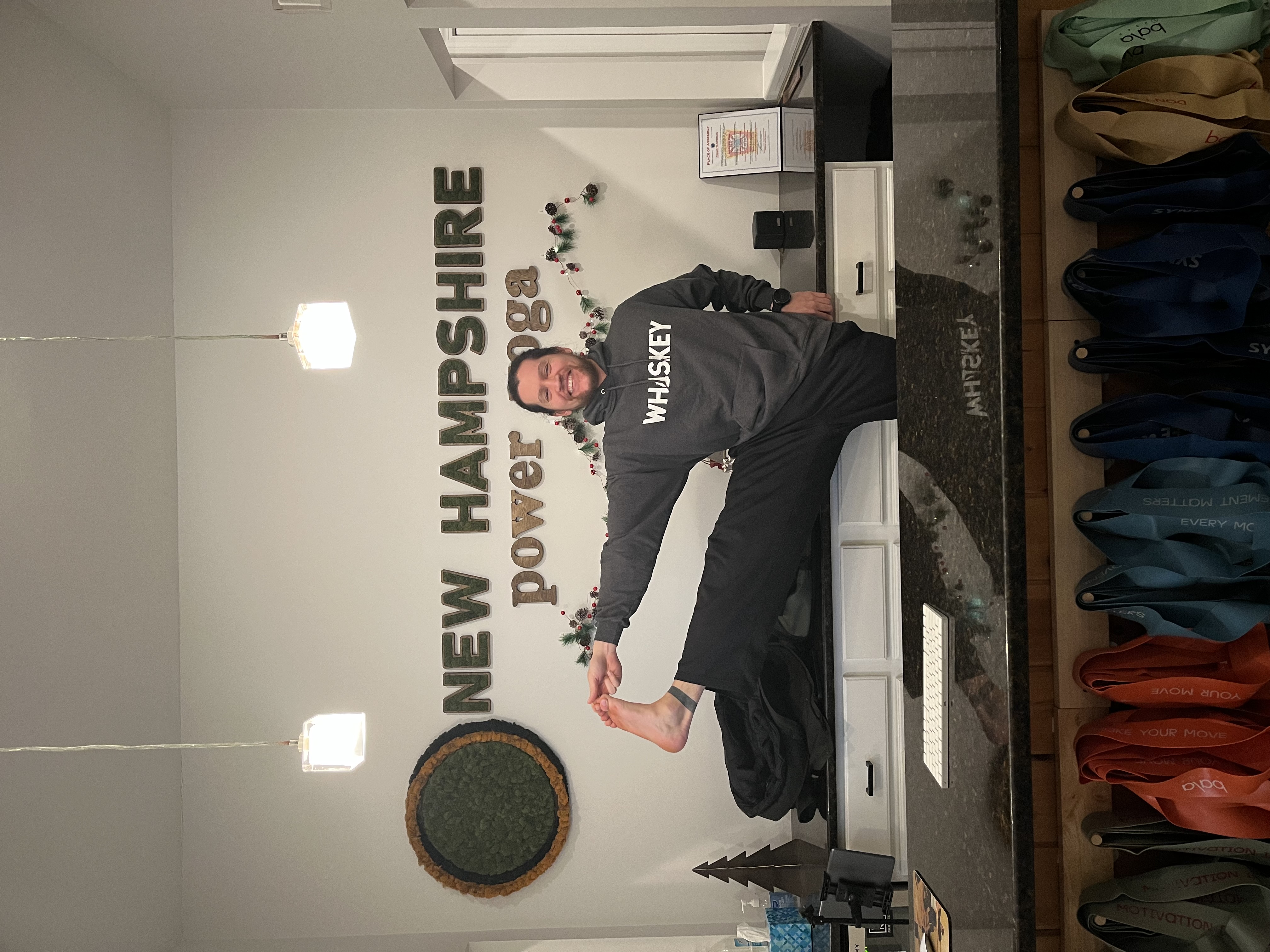 Tony Tenaglier balancing on one leg while holding his other leg extended upward, inside the New Hampshire Power Yoga studio