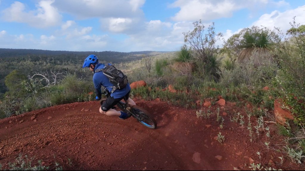 A mountain biker leaning into a turn on a red dirt trail in the Pilbara, illustrating how focused play and movement can restore energy.