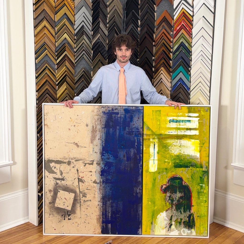 Lyall Penley in the framing studio holding framed artwork
