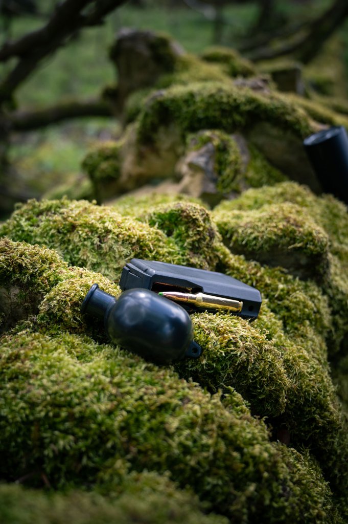 Stalking rifle magazine and ammunition on moss-covered rock — countryside sporting fieldcraft
