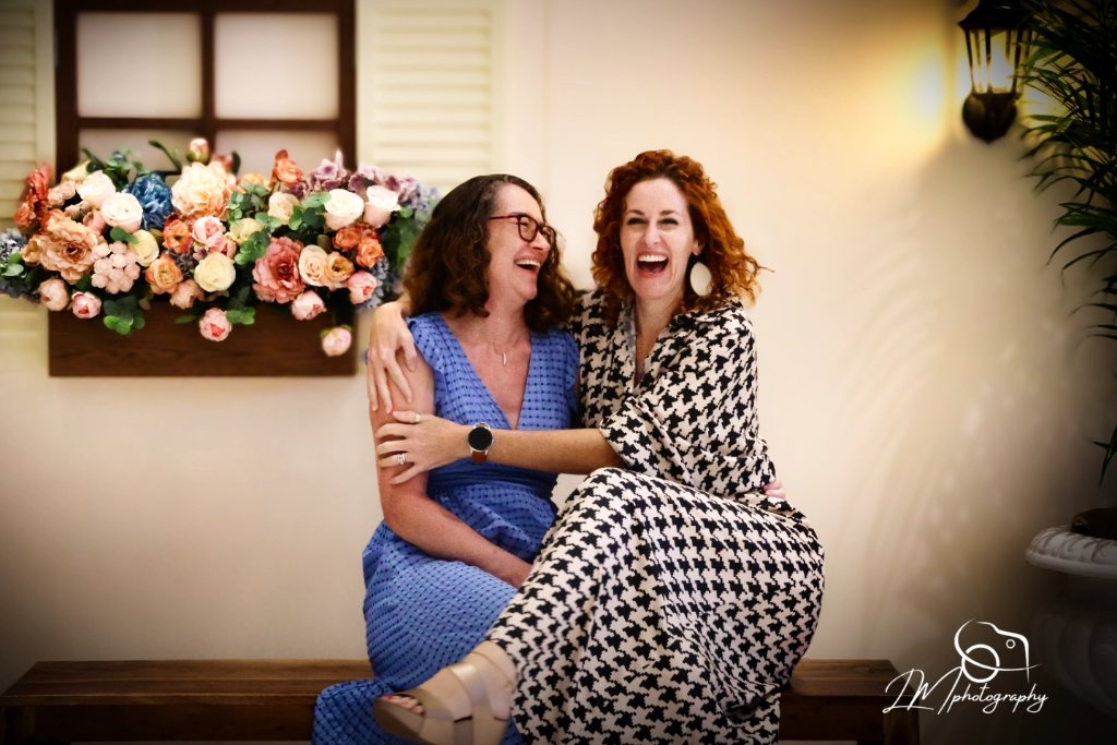 Two women laughing together at event with flower wall backdrop