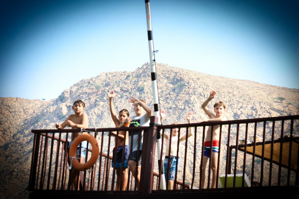 Children enjoying seaside event on dock with scenic mountain landscape, playful moments captured
