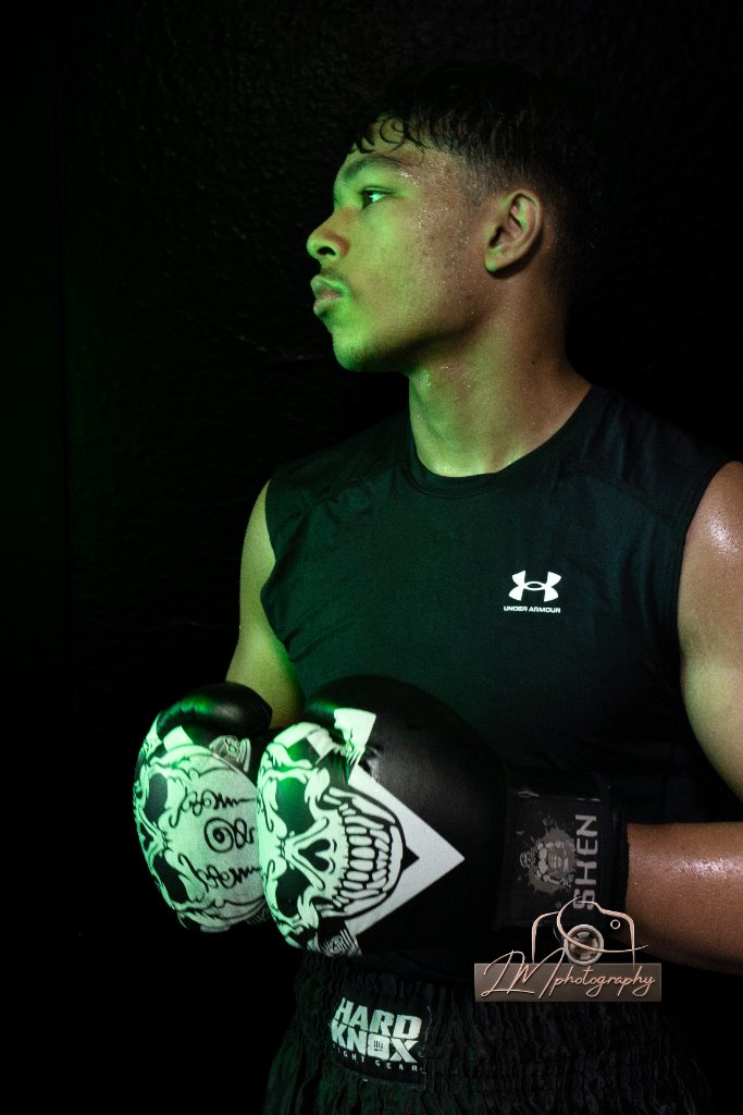 Boxer in profile with skull-graphic gloves under dramatic green lighting