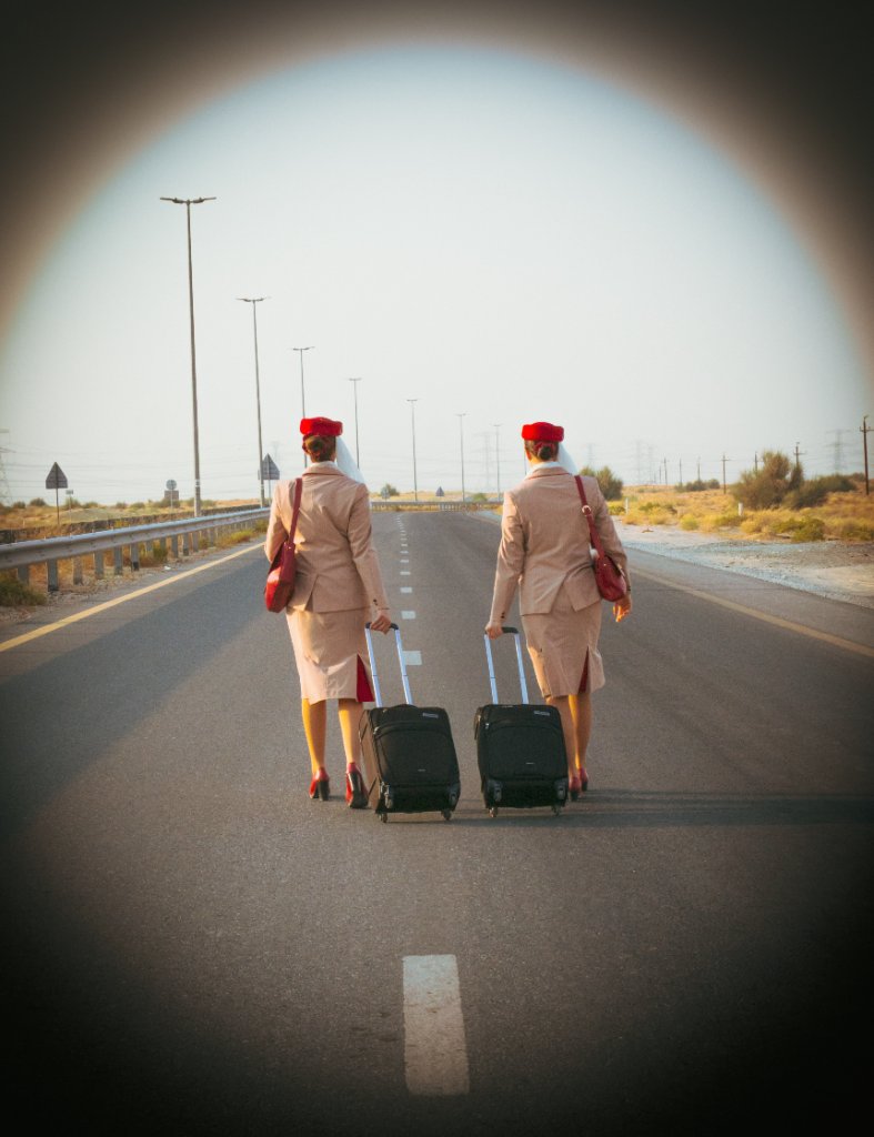 Two flight attendants walking away down a desert road with rolling suitcases