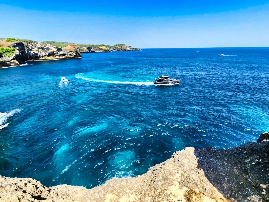 Elevated coastal view of turquoise waters with rocky cliffs and distant island with yacht
