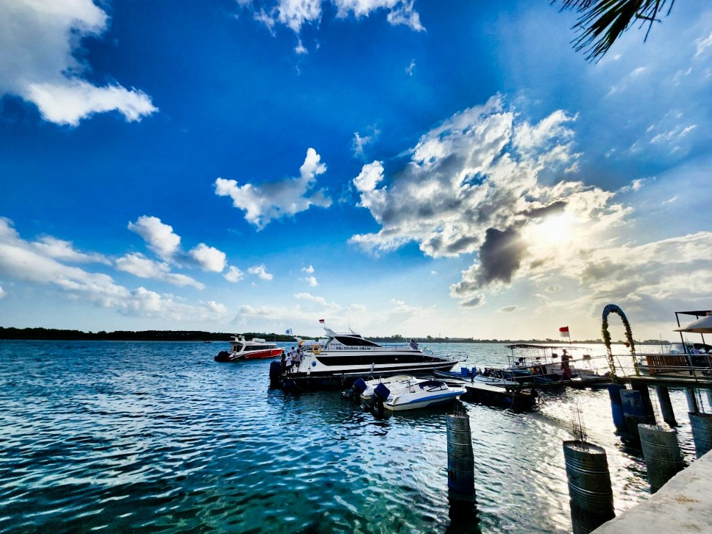 Serene marina with moored boats under dramatic sky with white clouds and palm trees