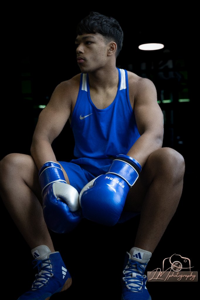 Boxer seated in blue Nike singlet with Phenom gloves looking off camera