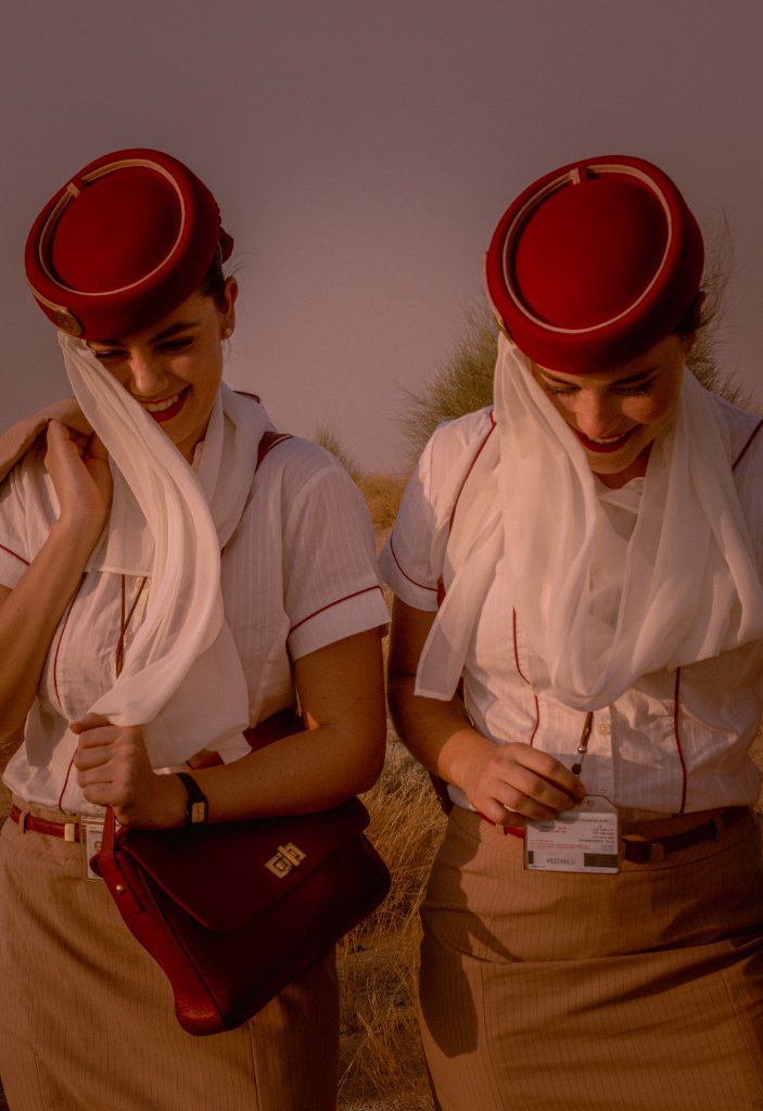 Two flight attendants from chest up smiling in the desert with red handbag and ID badge