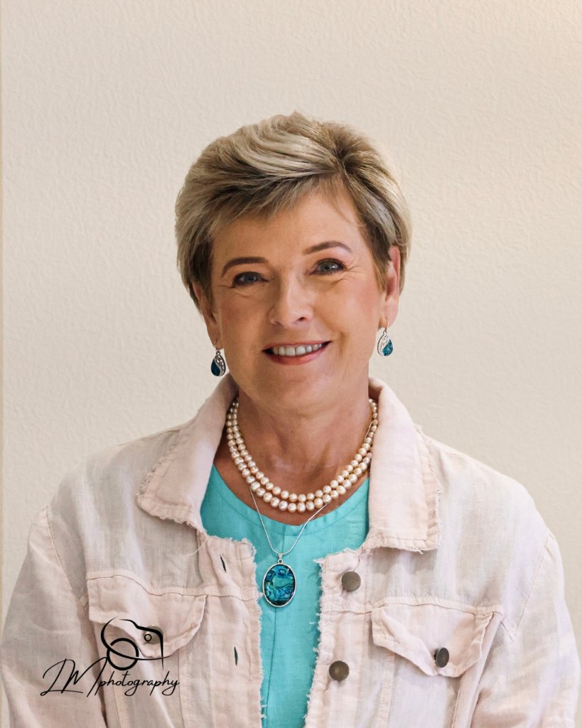 Professional portrait of woman with pearl necklace and turquoise top on neutral background