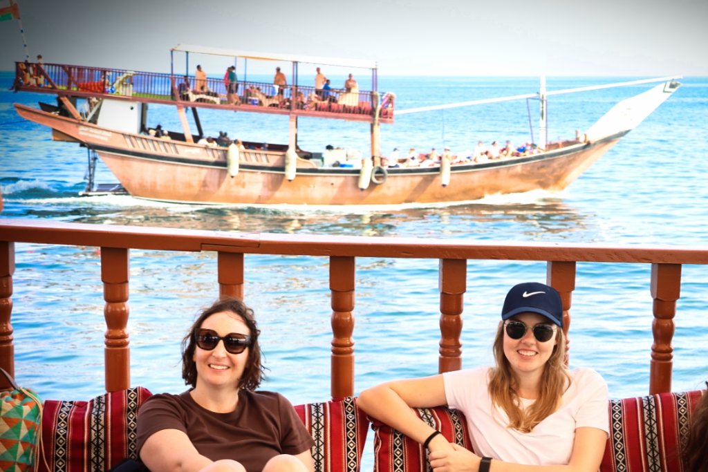 Joyful couple at beach event with traditional boats, clear waters and scenic backdrop