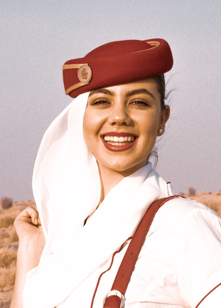 Smiling flight attendant in red pillbox hat and white scarf against a desert backdrop