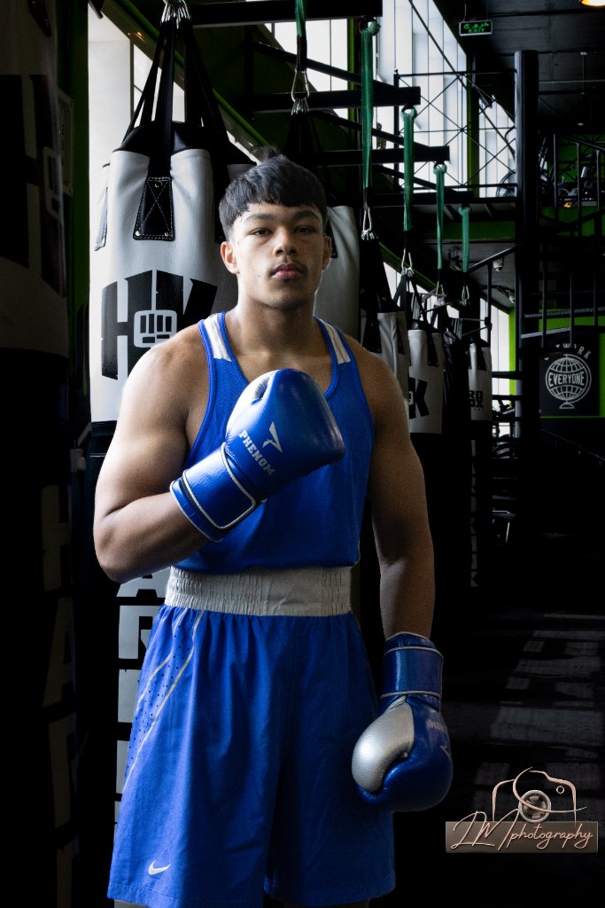 Boxer standing in blue Nike gear with Phenom gloves among punching bags