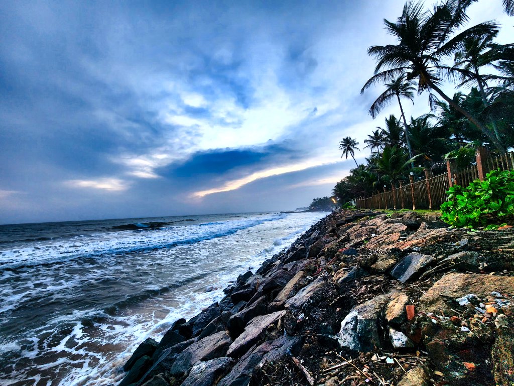 Tropical beach at dusk with palm trees, rocky shoreline and soft evening light over calm waters