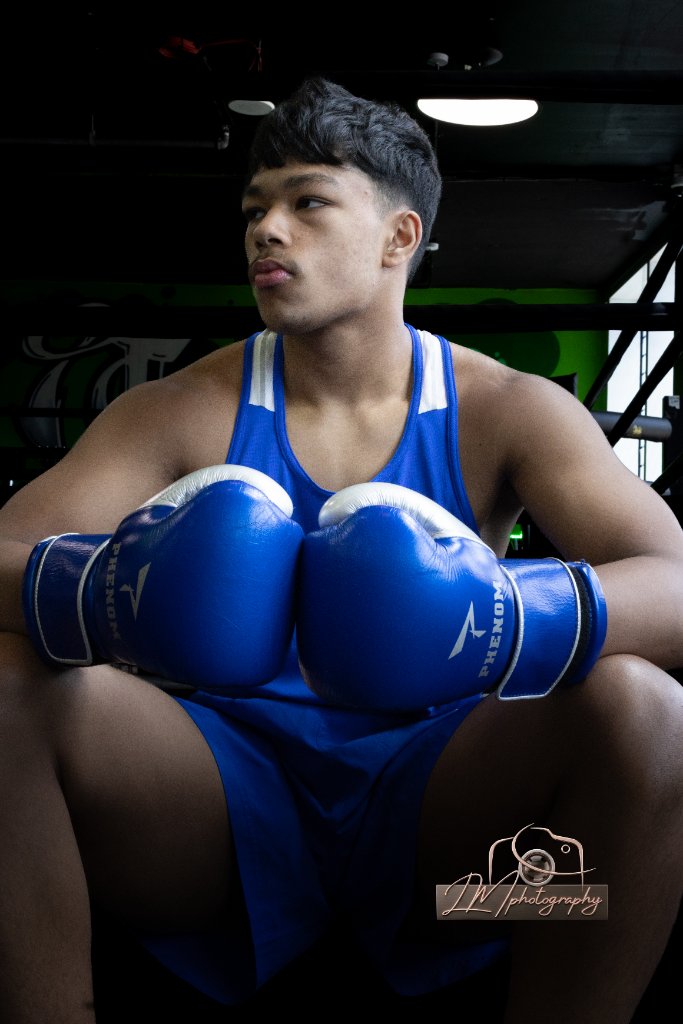 Boxer seated in blue tank top with Phenom gloves in dark gym