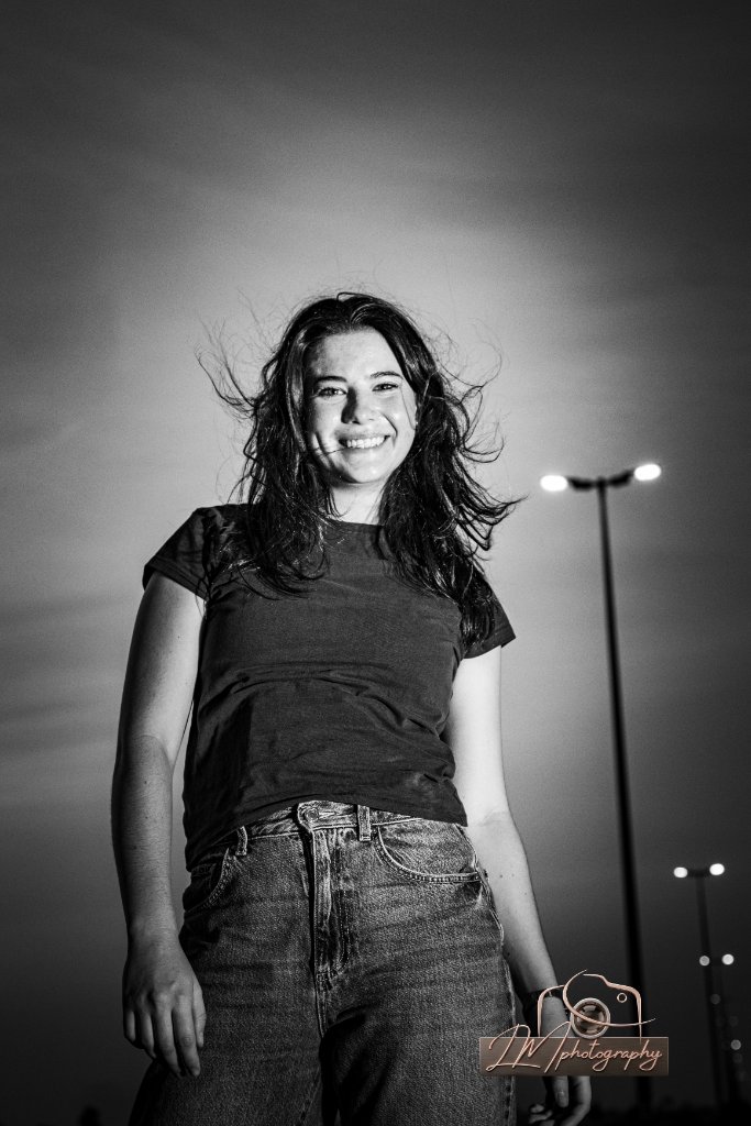 Black and white portrait of a smiling woman at dusk with streetlight lens flares