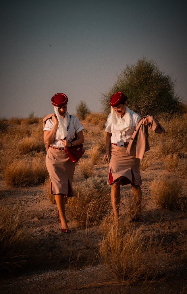 Two flight attendants walking side by side through desert terrain at golden hour