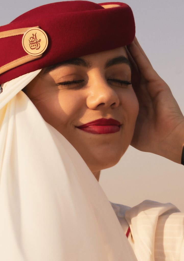 Close-up portrait of flight attendant with eyes closed touching her red hat in warm light