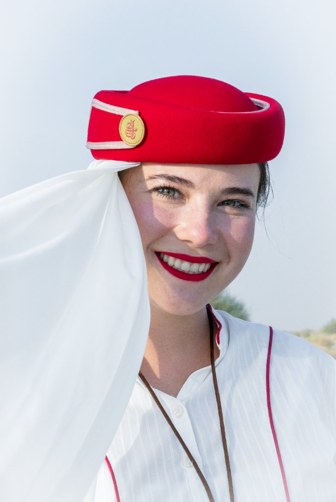 Head and shoulders portrait of a smiling flight attendant in red hat and white scarf