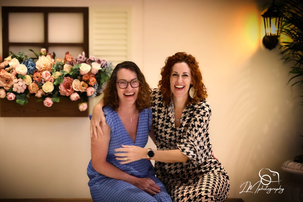 Two women smiling in front of colorful floral arrangement at event