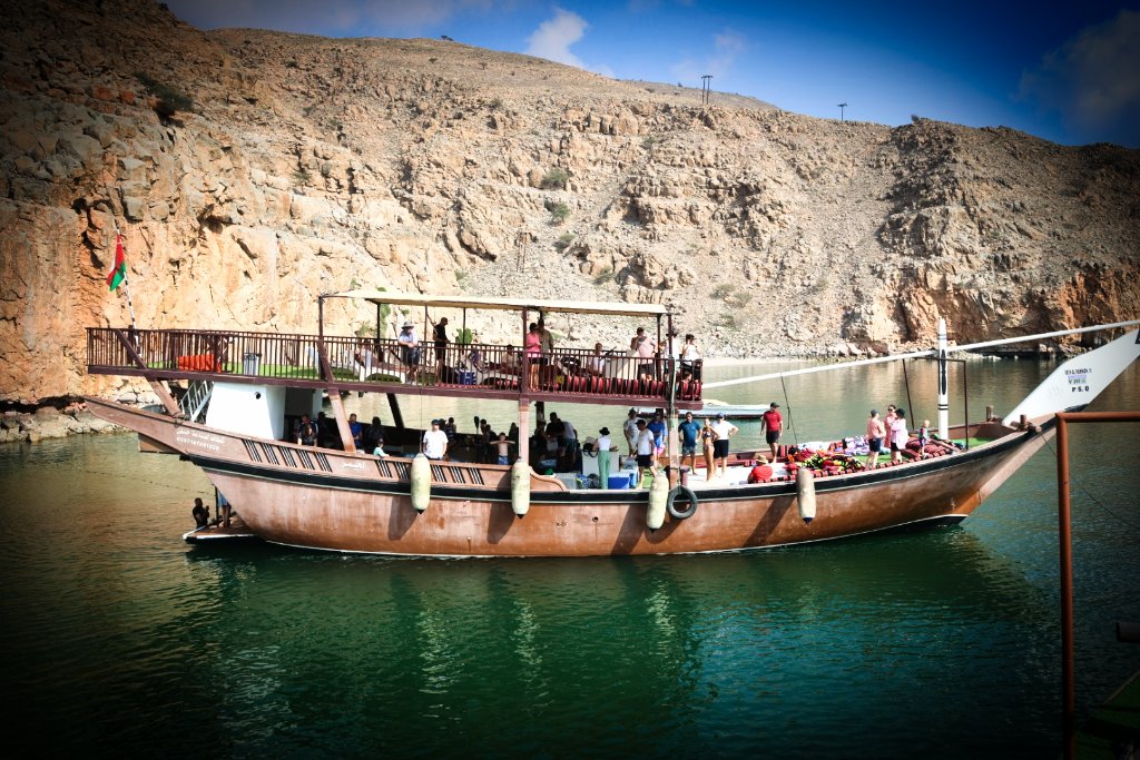 Large group of guests enjoying organized boat tour on scenic river with mountain backdrop