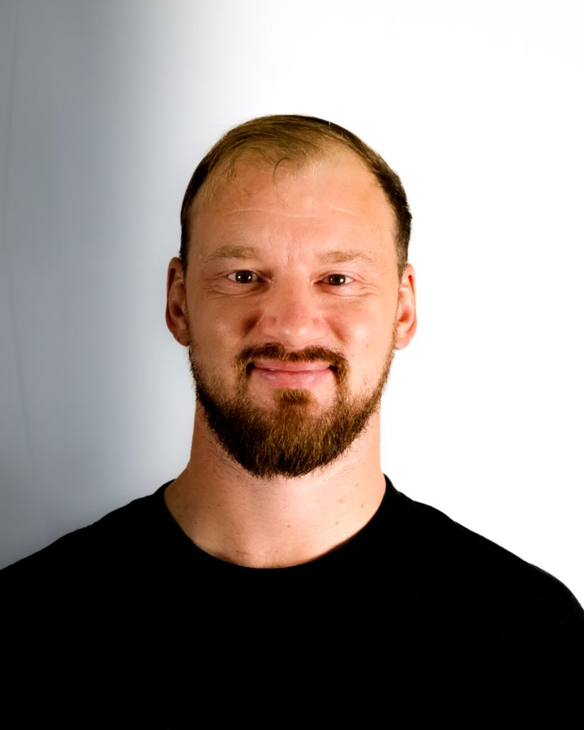 Head and shoulders portrait of man with full brown beard in black t-shirt against white studio background