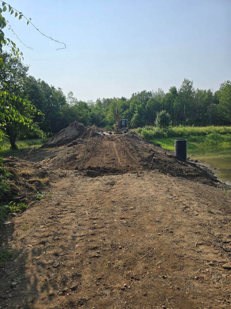 Excavation in progress — dam opened and new overflow standpipe installed, compaction lifts underway
