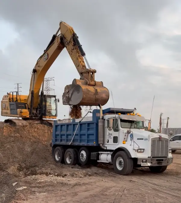 Excavator loading fill dirt into the bed of a dump truck