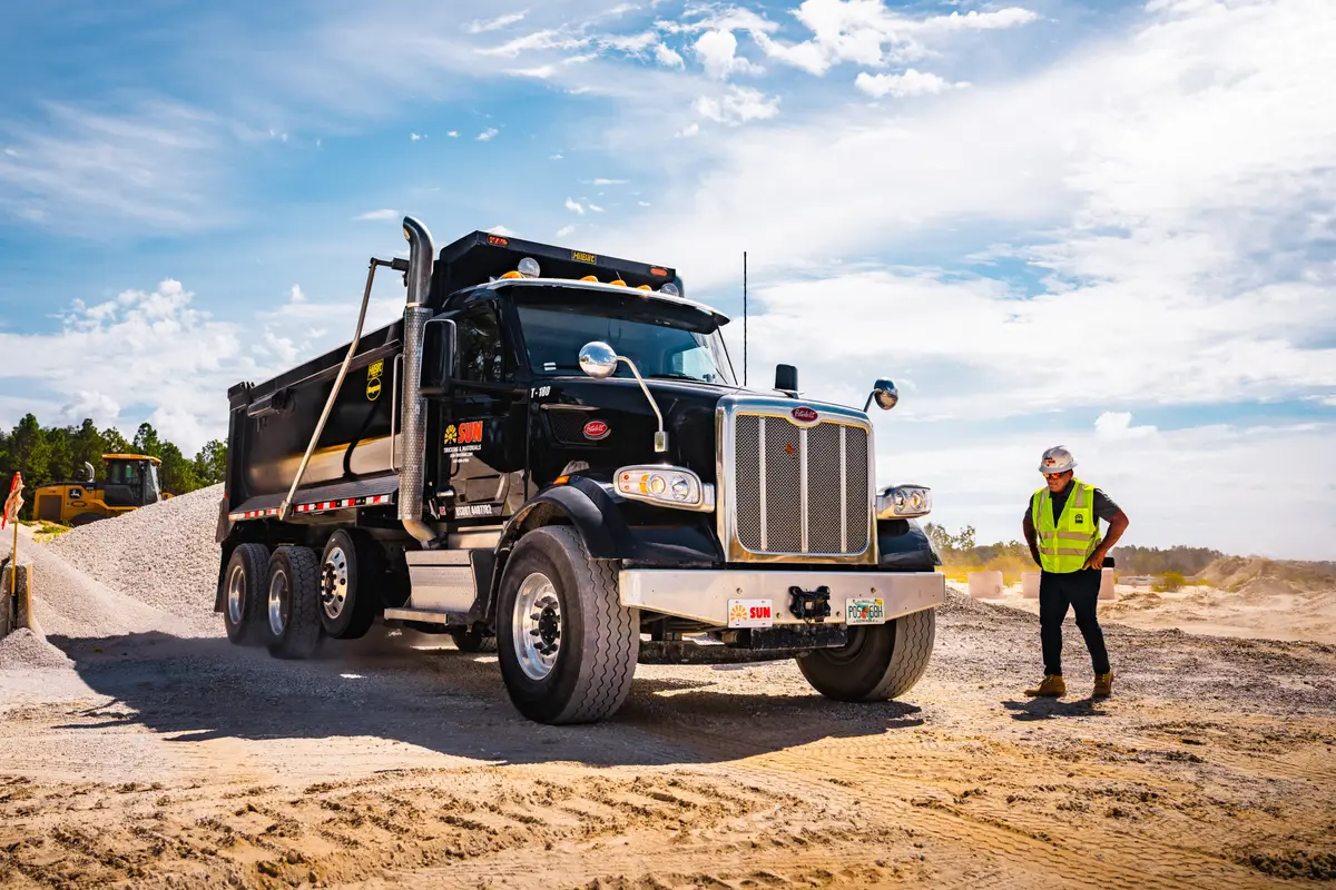 Sun Trucking driver in safety gear beside a dump truck