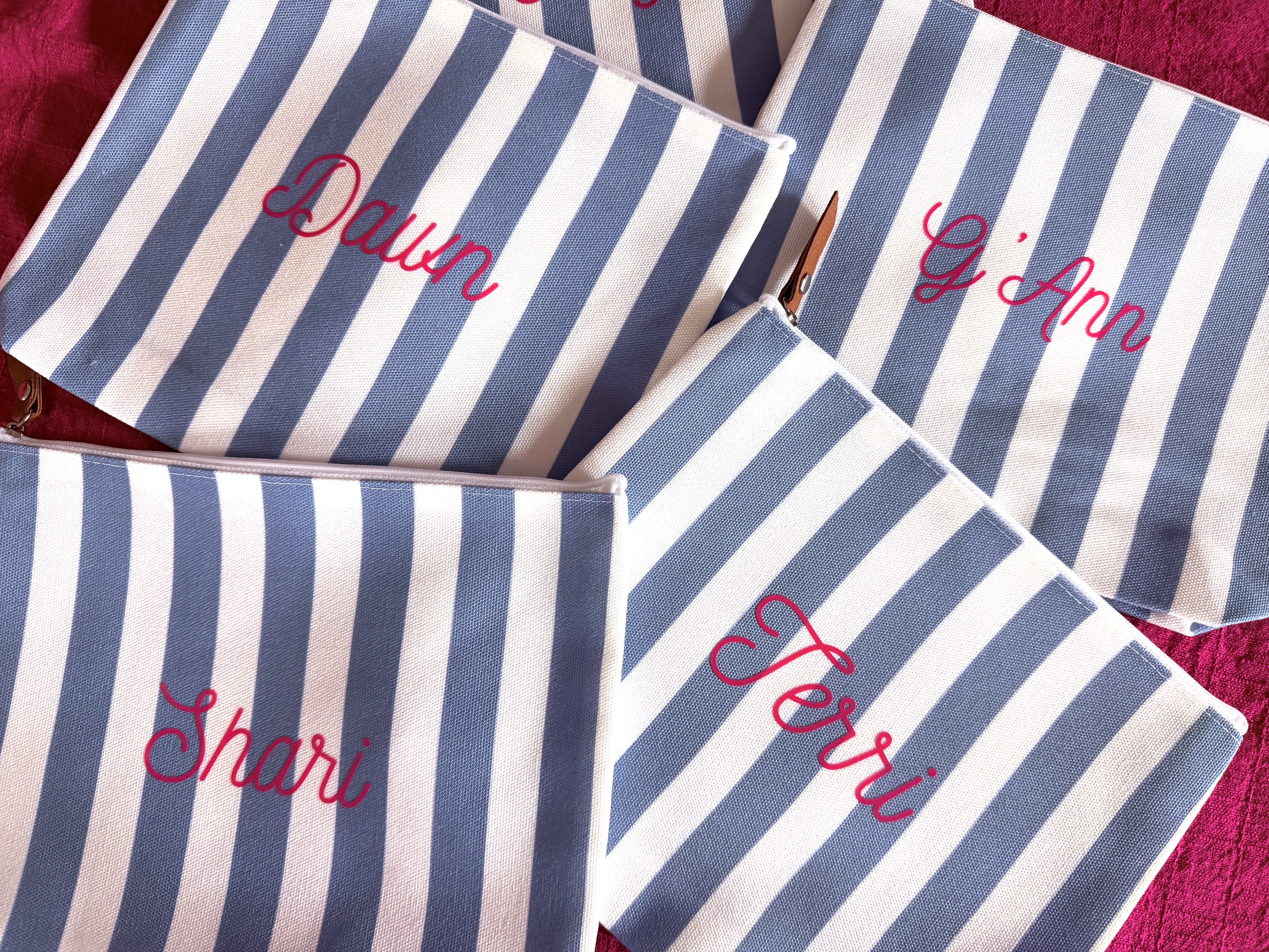Blue and white striped canvas makeup pouches personalized with names Dawn, G'Ann, Shari, and Terri in pink script