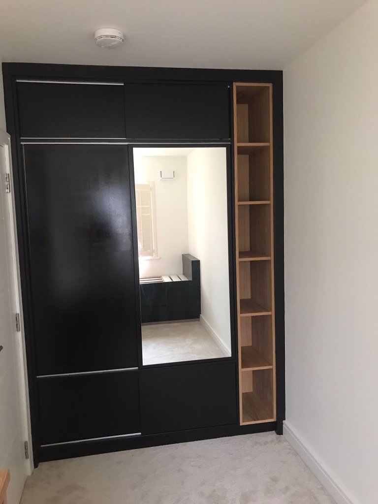 Dark fitted sliding wardrobe with mirror and oak shelving by HEFF