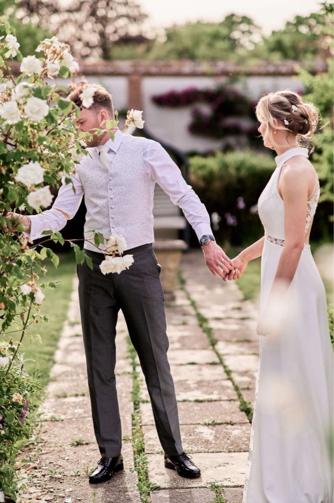 Bride and groom on a garden path by rose bushes