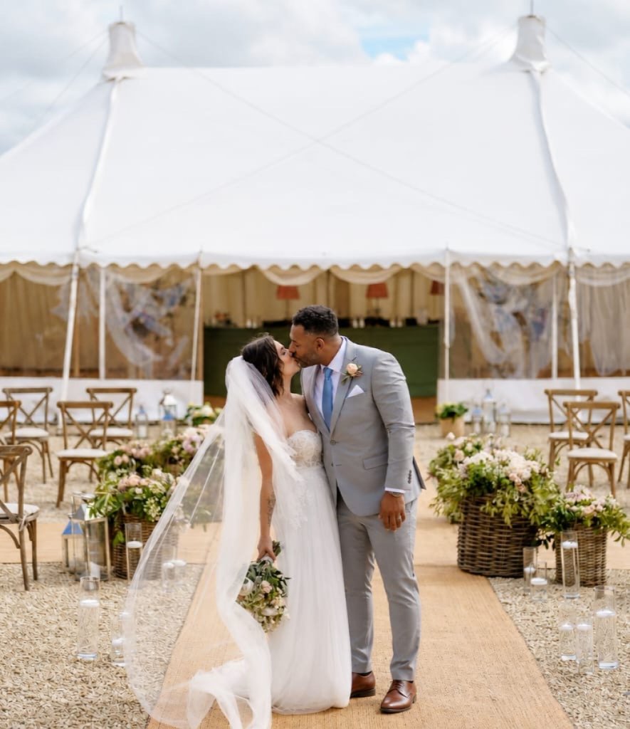 Bride and groom kissing on a pathway in front of a marquee