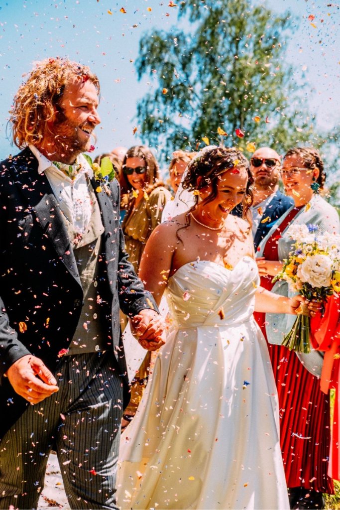 Bride and groom laughing through a shower of confetti